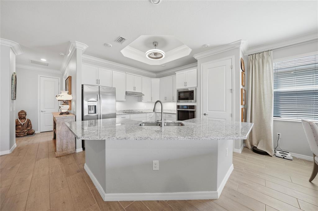 A kitchen features white cabinets, granite countertops, a central island, and light-colored wood-look flooring — 15039 BLACK CHERRY WAY, PUNTA GORDA, FL