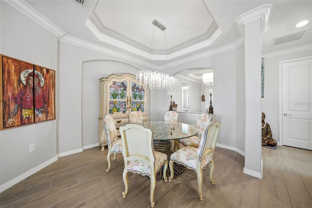 A dining room features a glass-top table, floral chairs, a crystal chandelier, and wood flooring — 15039 BLACK CHERRY WAY, PUNTA GORDA, FL