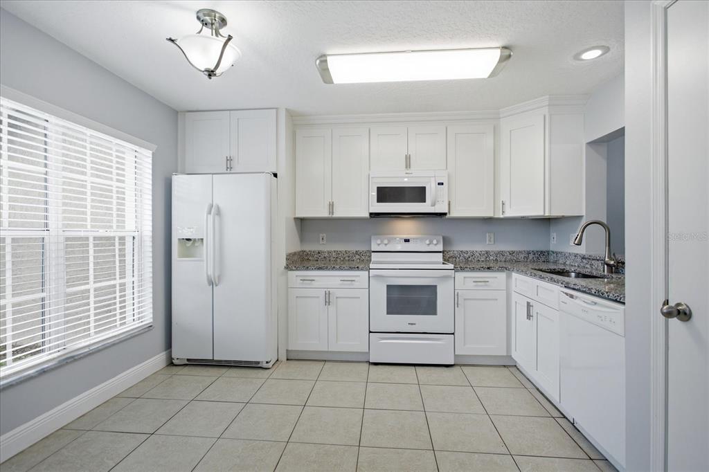 A kitchen with white cabinets, granite countertops, white appliances, and light-colored tile flooring — 2321 WATER VIEW LOOP, KISSIMMEE, FL