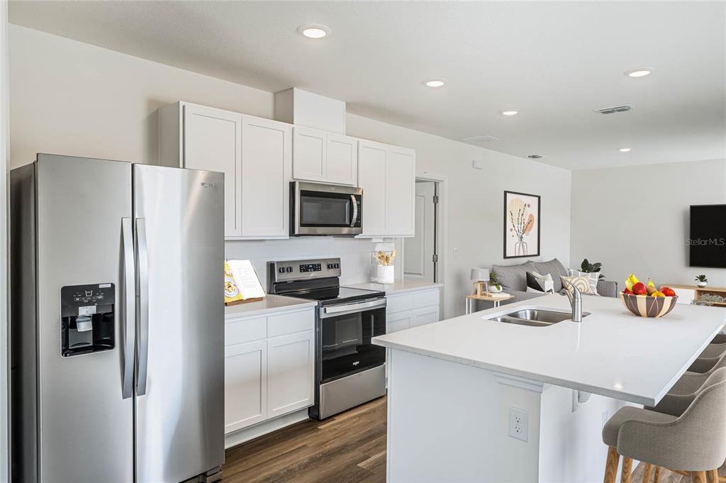 A modern kitchen features white cabinets, stainless steel appliances, and a large central island — 5130 CLUSIA DRIVE, APOPKA, FL