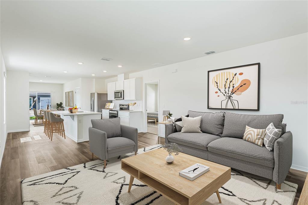 An open-concept living room and kitchen featuring gray furniture, wood-look flooring, and a patterned rug — 5130 CLUSIA DRIVE, APOPKA, FL