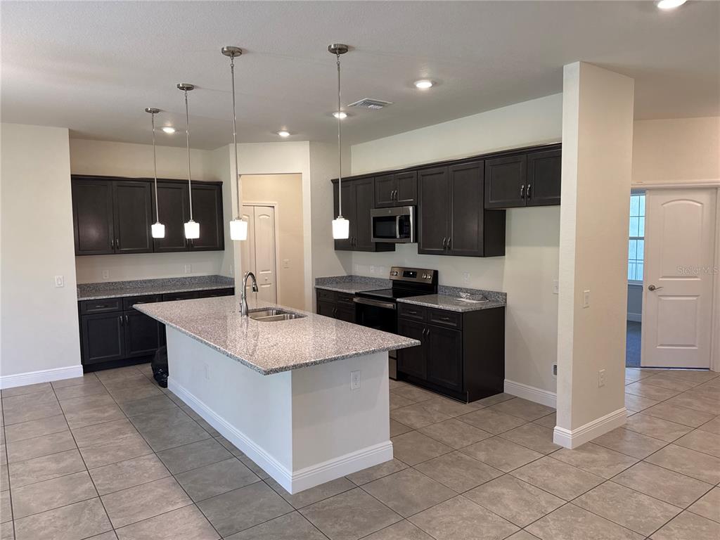 A kitchen features dark wood cabinets, granite countertops, a central island, and tile flooring — 4698 ADDLEY AVENUE, NORTH PORT, FL