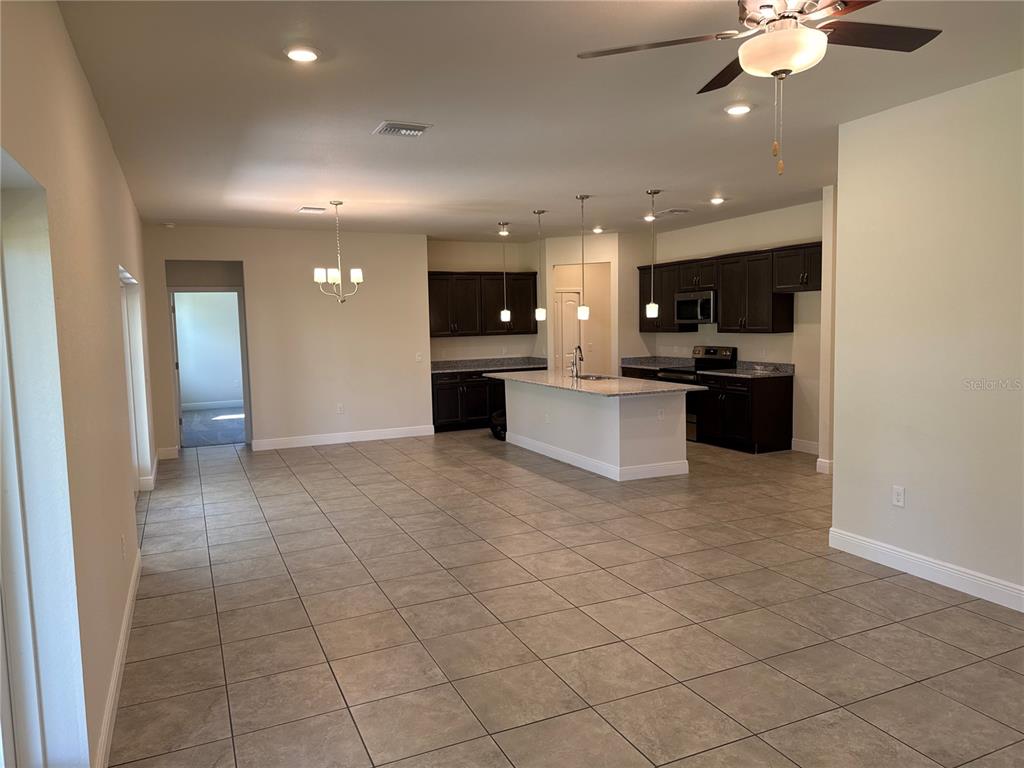 An open-concept kitchen features dark cabinetry, a granite-topped island, and tile flooring — 4698 ADDLEY AVENUE, NORTH PORT, FL