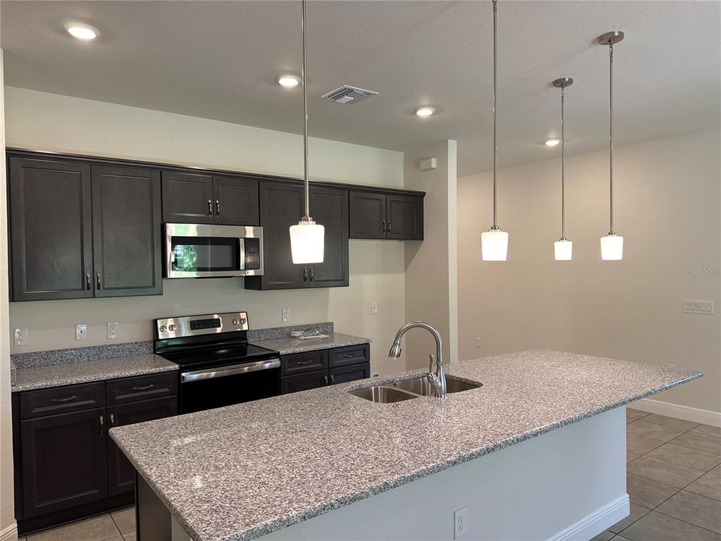 A kitchen features dark wood cabinets, granite countertops, a center island, and three pendant lights — 4698 ADDLEY AVENUE, NORTH PORT, FL