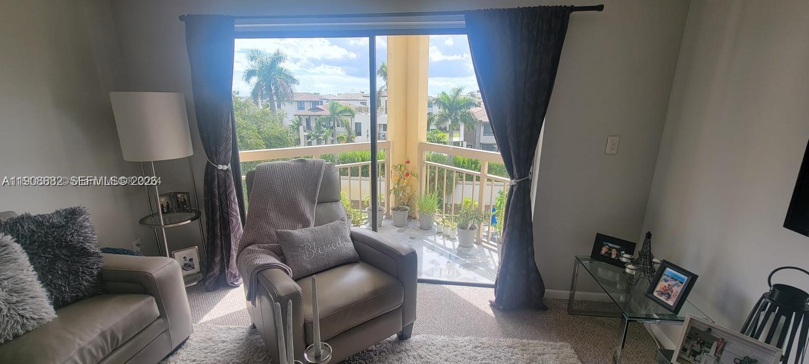 A living room features a leather armchair, a sliding glass door, and a balcony with plants — 8290 Lake Dr # 426, Doral FL 33166, DORAL, FL