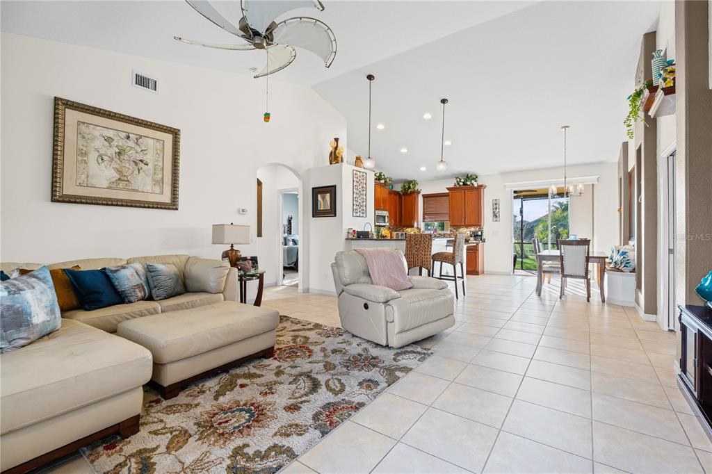 An open-concept living room and kitchen feature tile floors, vaulted ceilings, and neutral furniture — 12807 24TH STREET CIRCLE E, PARRISH, FL