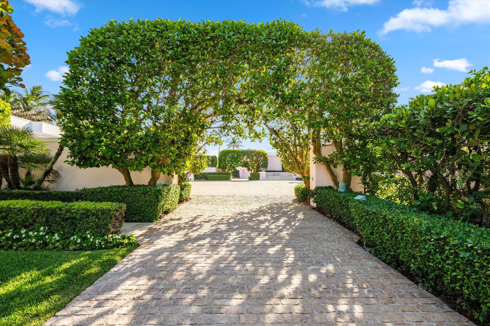 A stone driveway leads through a lush green tree archway toward a private residence — 911 N Ocean Boulevard, Palm Beach FL 33480, PALM BEACH, FL