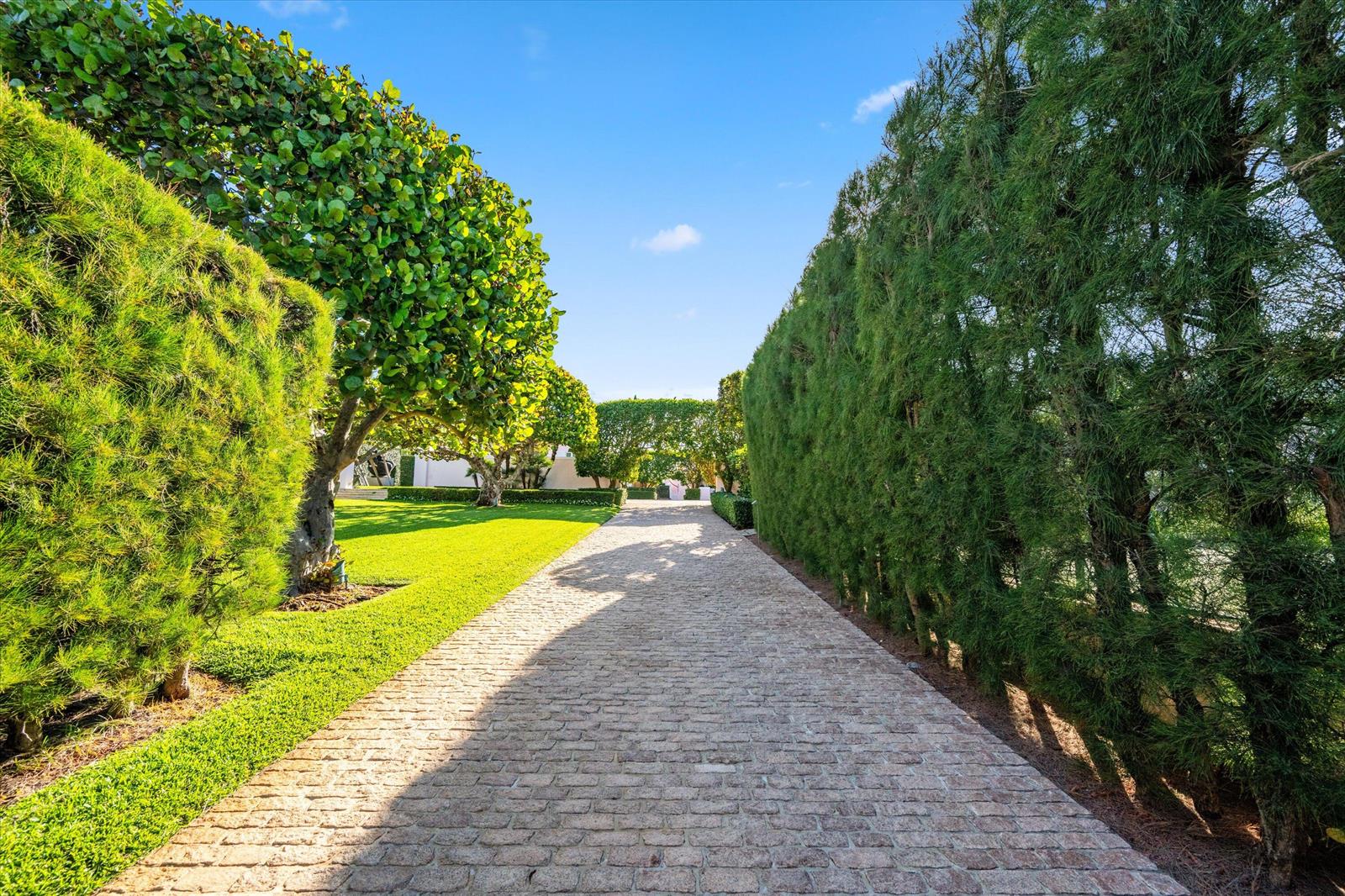 A stone driveway leads toward a house, flanked by manicured hedges and a green lawn — 911 N Ocean Boulevard, Palm Beach FL 33480, PALM BEACH, FL