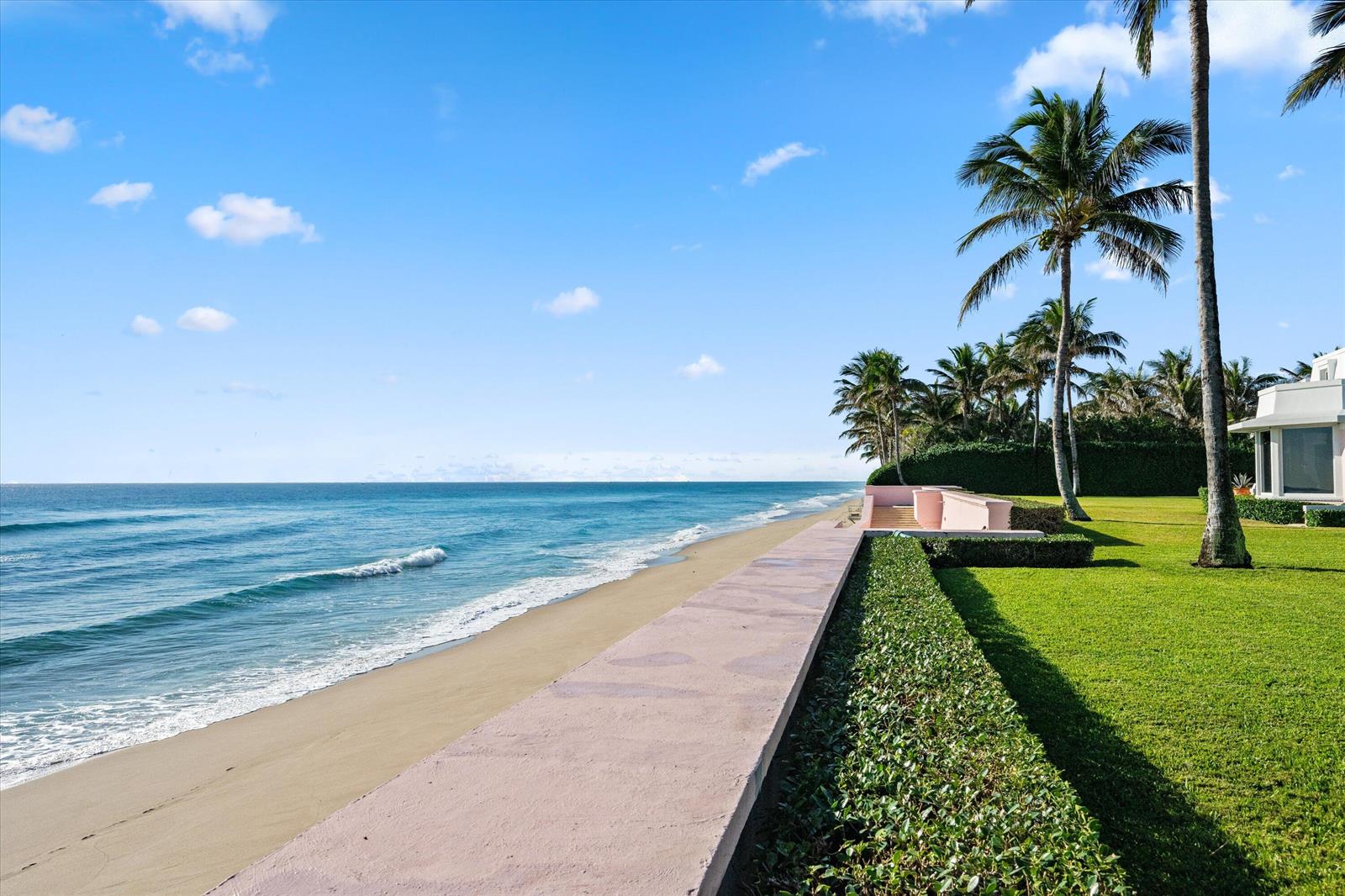 A grassy lawn with palm trees borders a concrete seawall overlooking a sandy beach and ocean — 911 N Ocean Boulevard, Palm Beach FL 33480, PALM BEACH, FL
