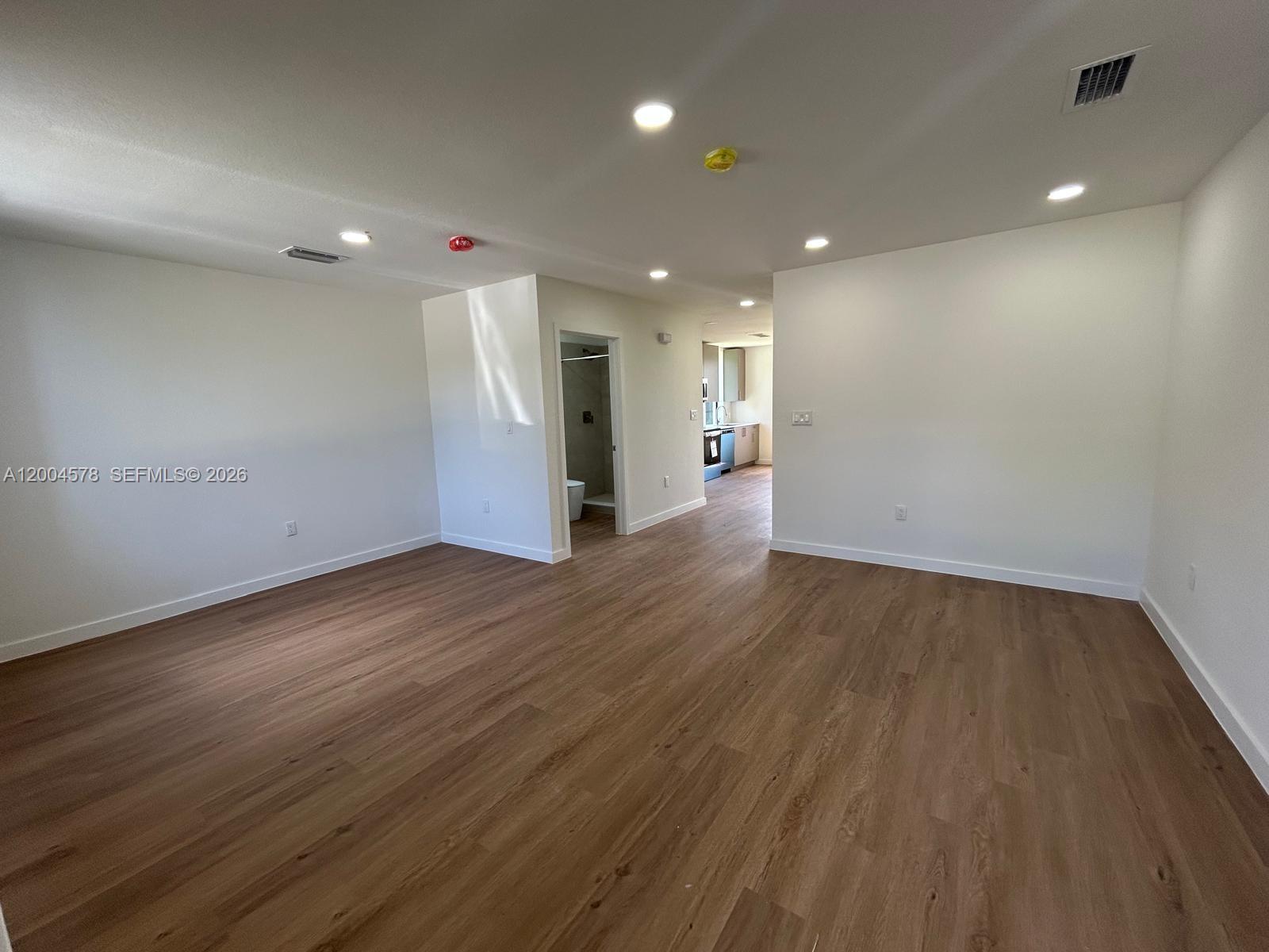 An empty room features light wood-look flooring, white walls, recessed lighting, and a doorway — 12554 SW 194th St # 0, Miami FL 33177, MIAMI, FL
