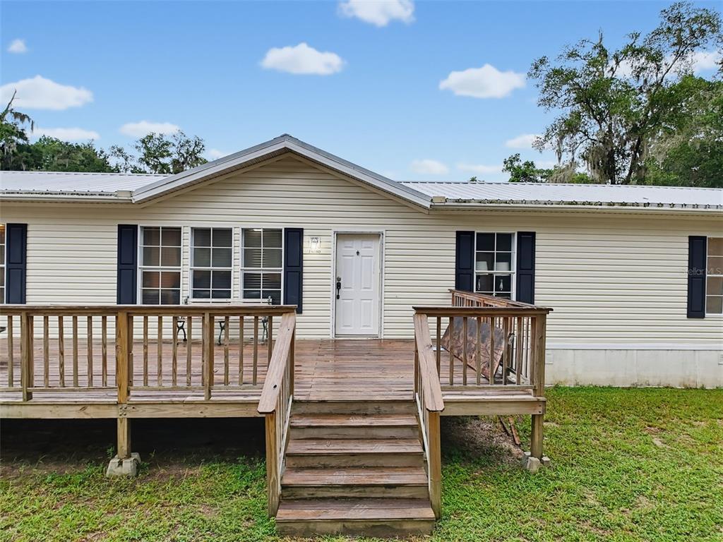 A single-story house with light siding, dark shutters, and a wooden deck with stairs — 14080 SE 122ND LANE ROAD, OCKLAWAHA, FL