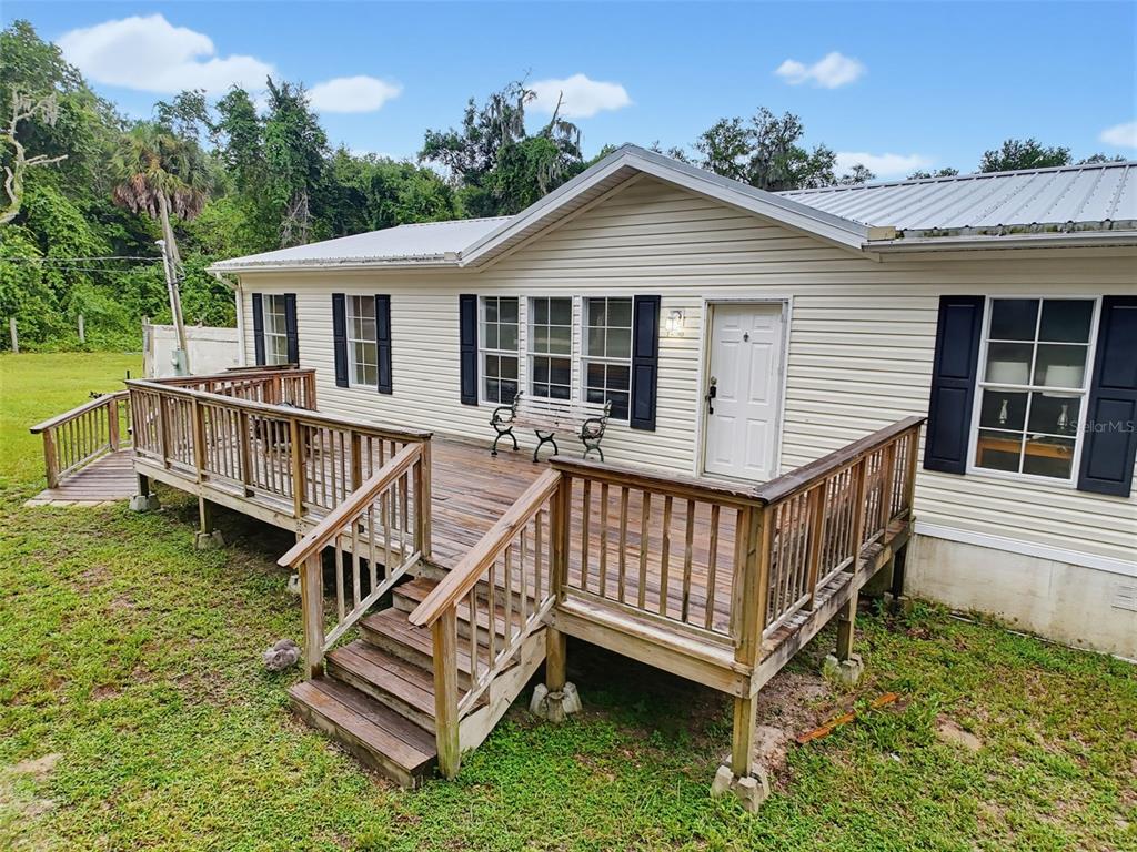 A single-story house with light siding, a metal roof, and a large wooden deck — 14080 SE 122ND LANE ROAD, OCKLAWAHA, FL