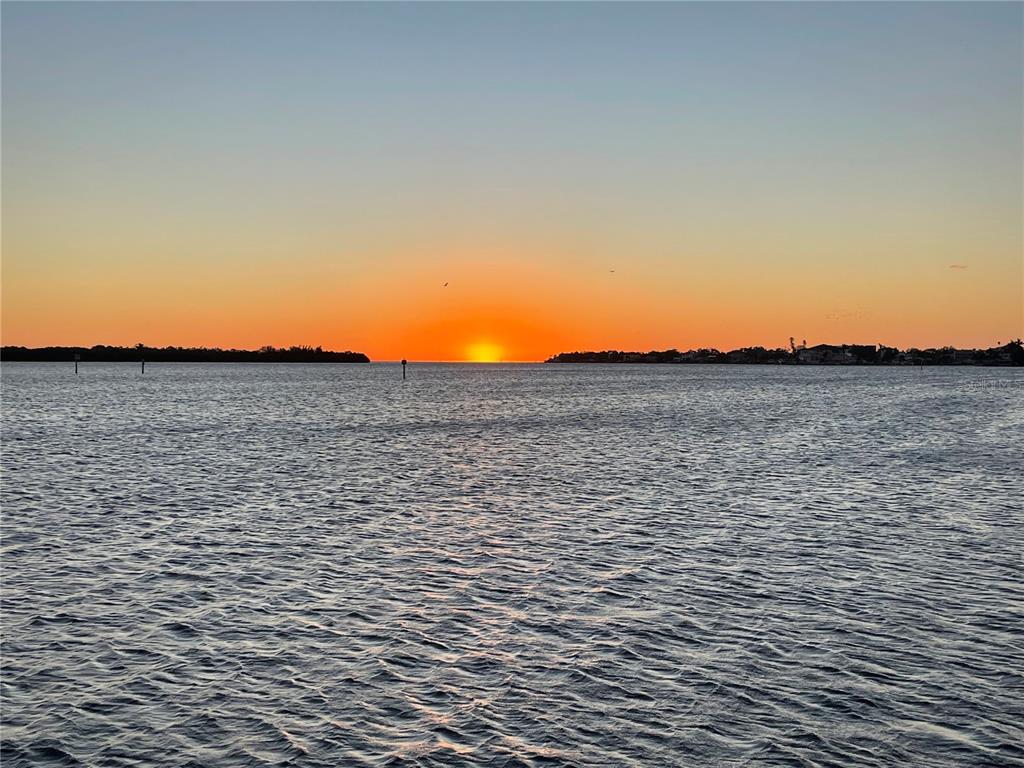 A vibrant sunset reflects over a calm body of water with a distant treeline — 6151 BAYOU GRANDE BOULEVARD NE, ST PETERSBURG, FL