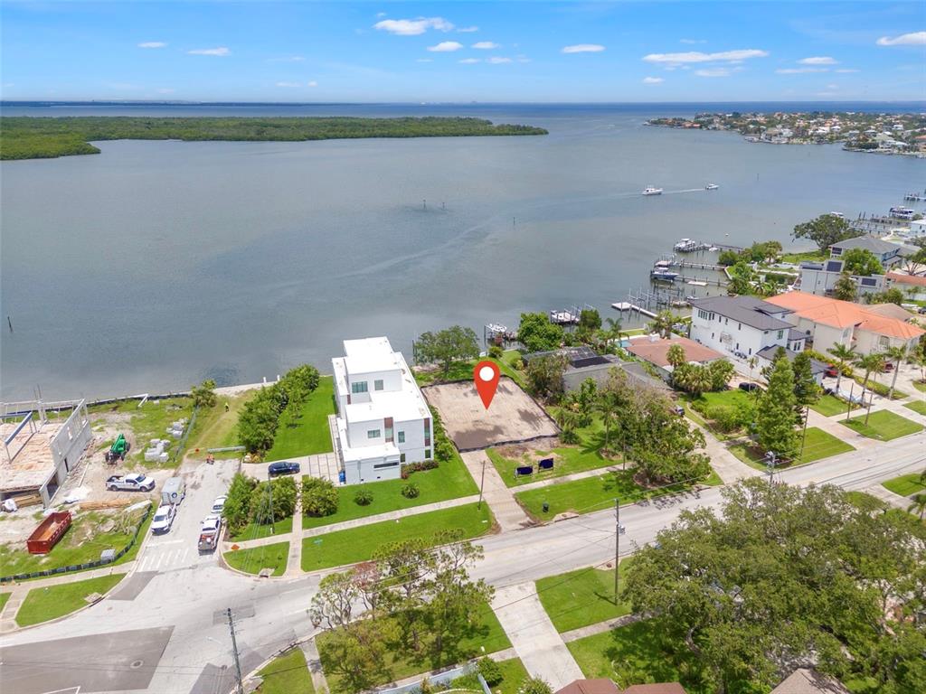 An aerial view shows a vacant waterfront lot next to a modern white house — 6151 BAYOU GRANDE BOULEVARD NE, ST PETERSBURG, FL