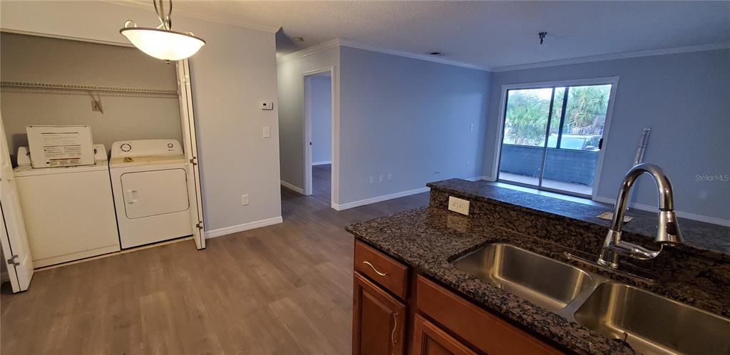 A kitchen with granite countertops and a sink overlooks a living area with laundry appliances — 10263 GANDY BOULEVARD N UNIT 403, ST PETERSBURG, FL