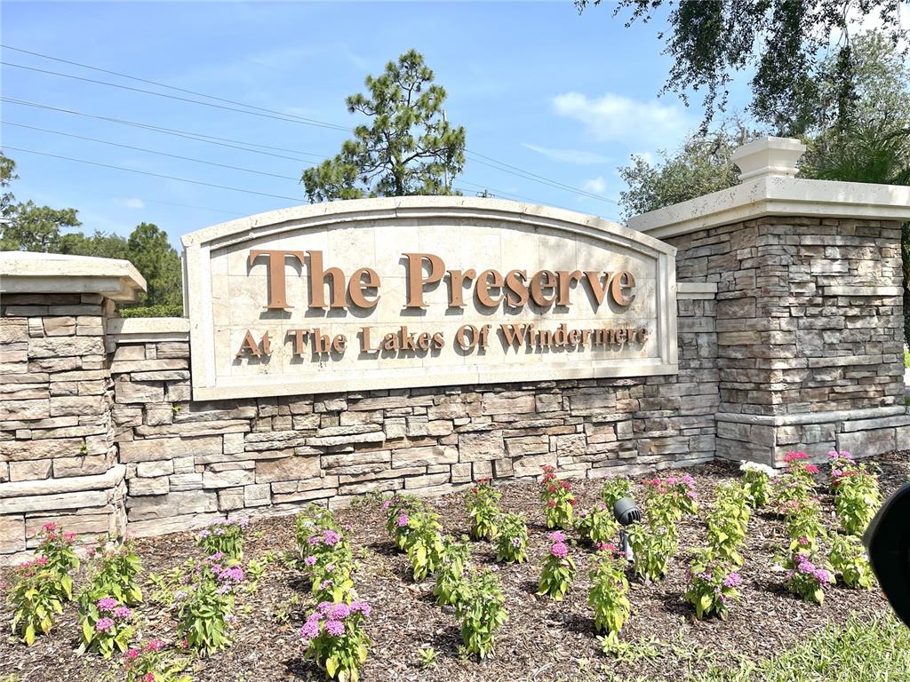 A stone monument sign displays the name of the community surrounded by pink flowering plants — 8321 GREENBANK BOULEVARD, WINDERMERE, FL