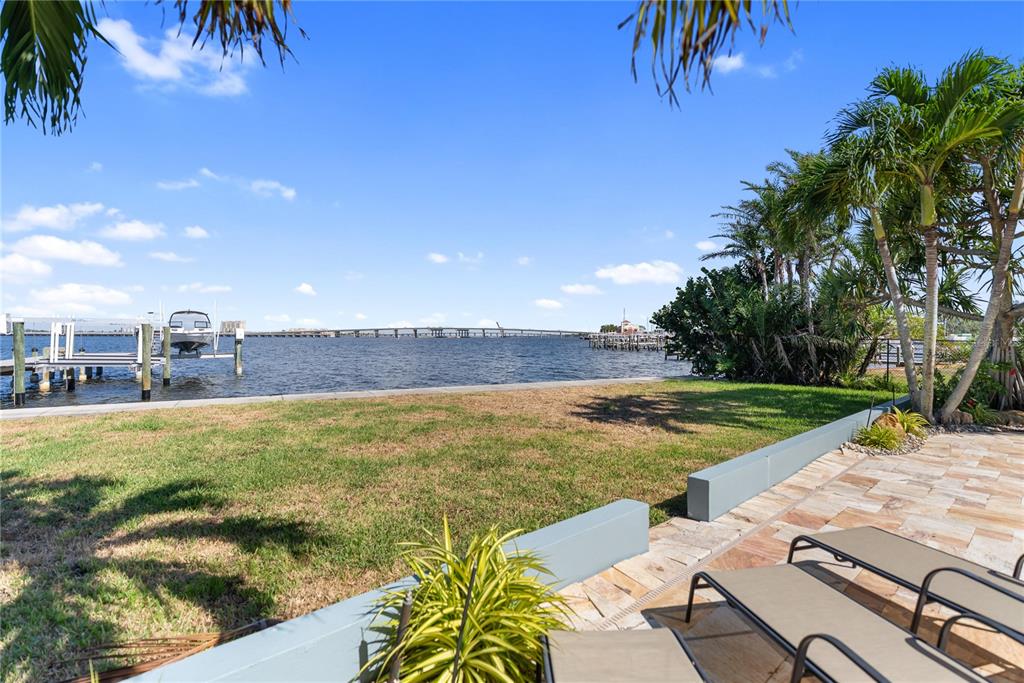 A grassy backyard overlooks a bay with a boat lift and a distant bridge — 1710 POINT PLEASANT AVENUE W, BRADENTON, FL