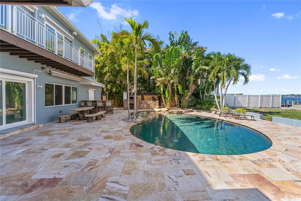 A backyard patio features a swimming pool, outdoor bar, and palm trees near the water — 1710 POINT PLEASANT AVENUE W, BRADENTON, FL