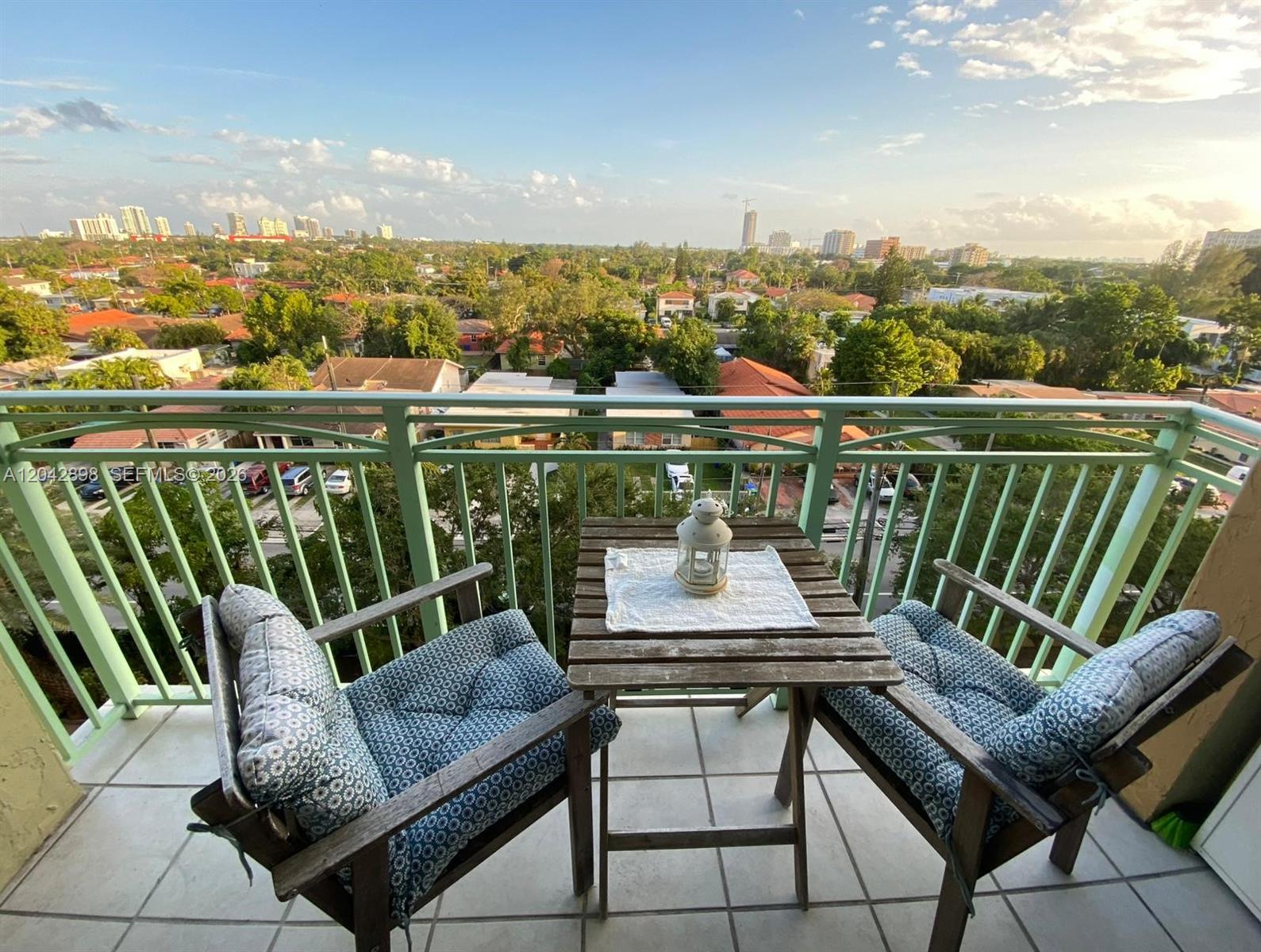 A balcony features two wooden chairs with patterned cushions and a small table overlooking trees — 3500 Coral Way # 707, Miami FL 33145, MIAMI, FL