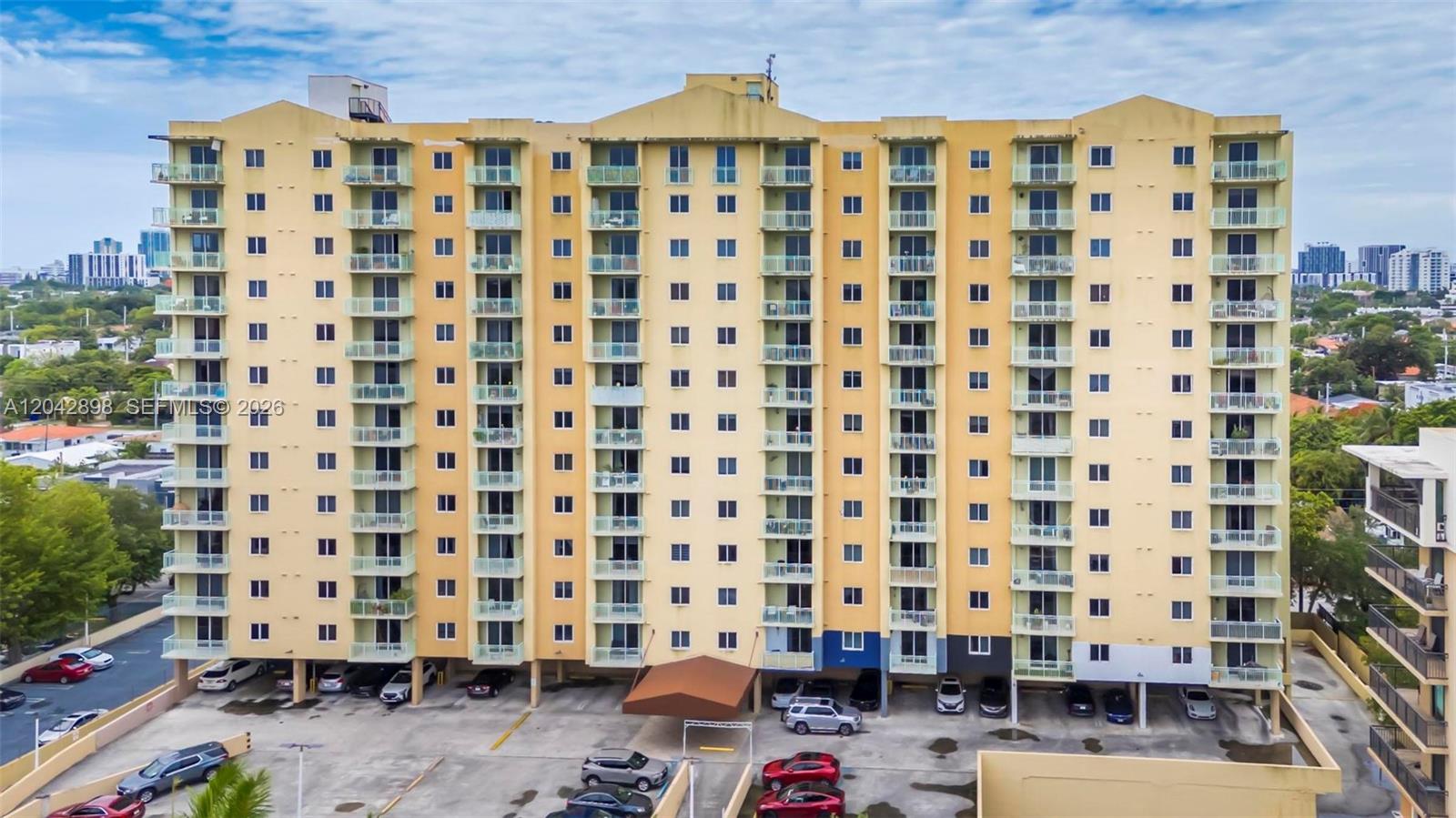 An exterior view of a multi-story yellow apartment building with balconies and a parking lot — 3500 Coral Way # 707, Miami FL 33145, MIAMI, FL