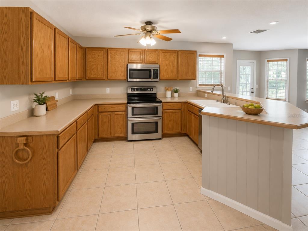 A kitchen features oak cabinets, stainless steel appliances, beige countertops, and light tile flooring — 4104 QUAIL NEST COURT, ST CLOUD, FL
