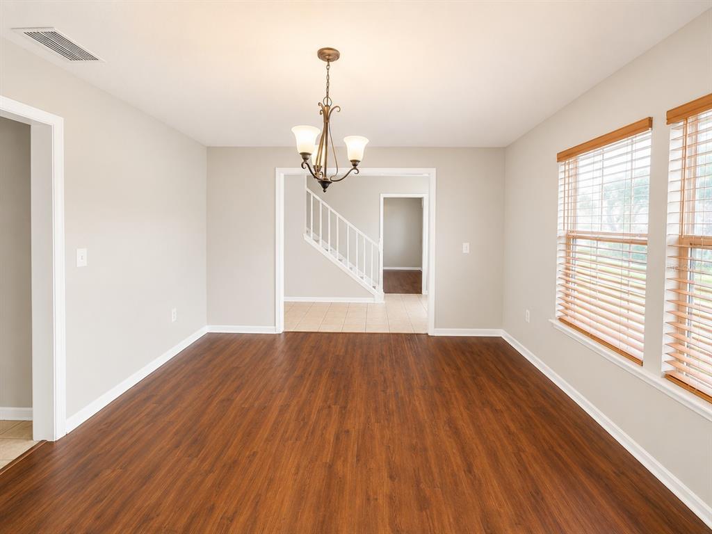 An empty dining room features wood-look flooring, light gray walls, and a hanging chandelier — 4104 QUAIL NEST COURT, ST CLOUD, FL