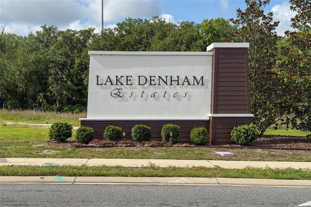 A white and brown monument sign for Lake Denham Estates stands near a grassy area — 3968 GADWALL PLACE, LEESBURG, FL