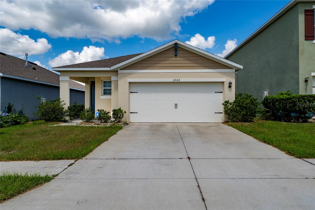 A single-story house with a beige stucco exterior, a two-car garage, and a concrete driveway — 3968 GADWALL PLACE, LEESBURG, FL