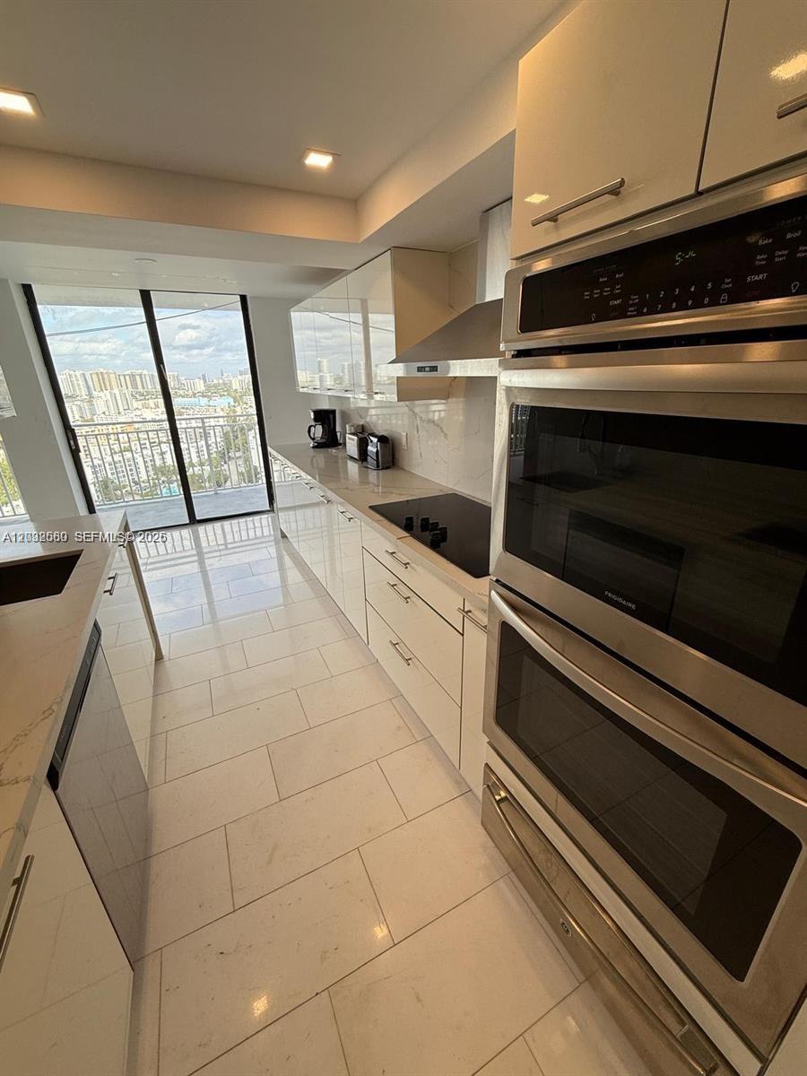 A modern kitchen features white glossy cabinets, stainless steel double ovens, and a balcony view — SUNNY ISLES BEACH, FL