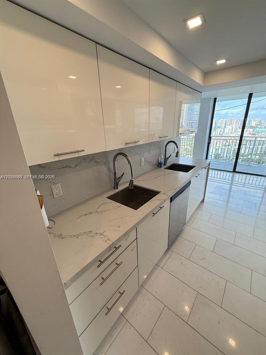 A modern kitchen features white high-gloss cabinets, quartz countertops, and a balcony view — SUNNY ISLES BEACH, FL