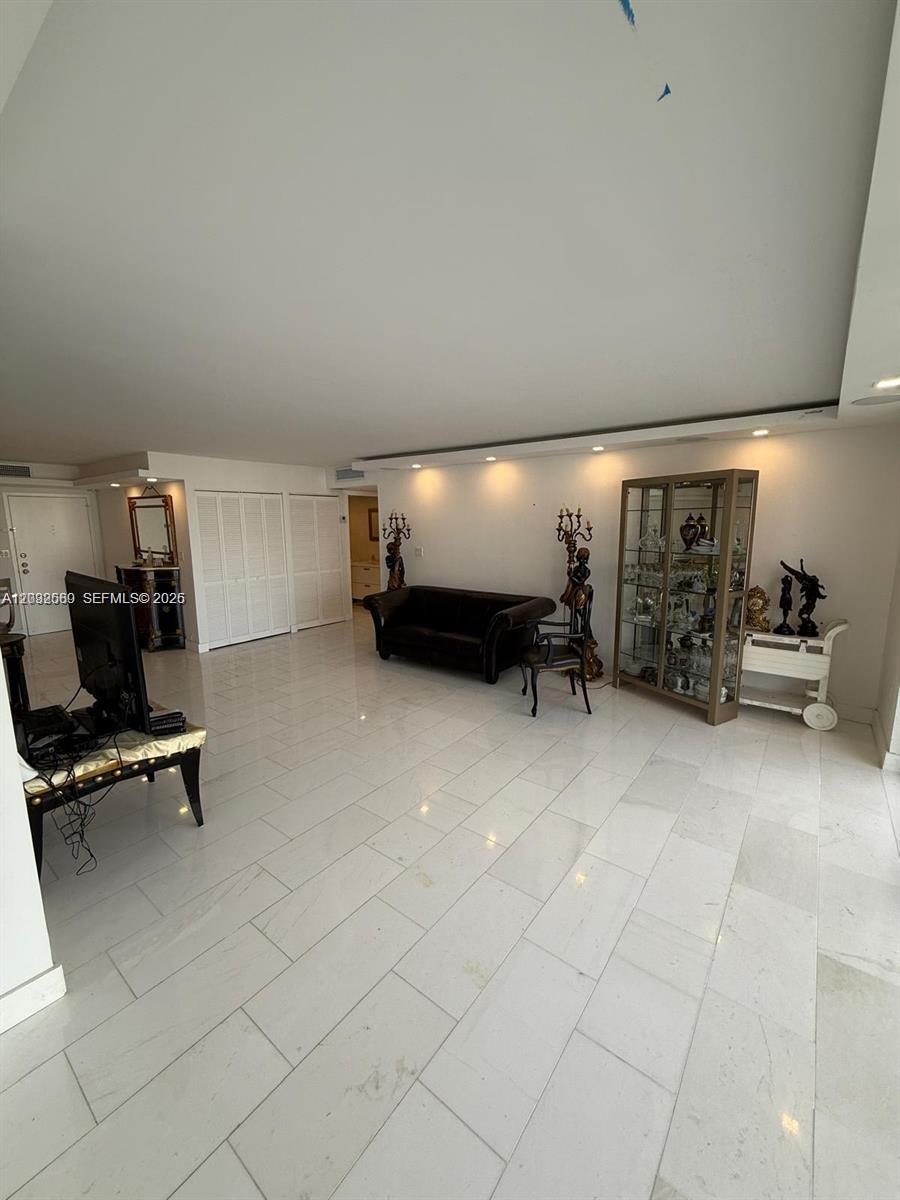 A spacious living room features white tile flooring, recessed lighting, and a dark velvet sofa — SUNNY ISLES BEACH, FL