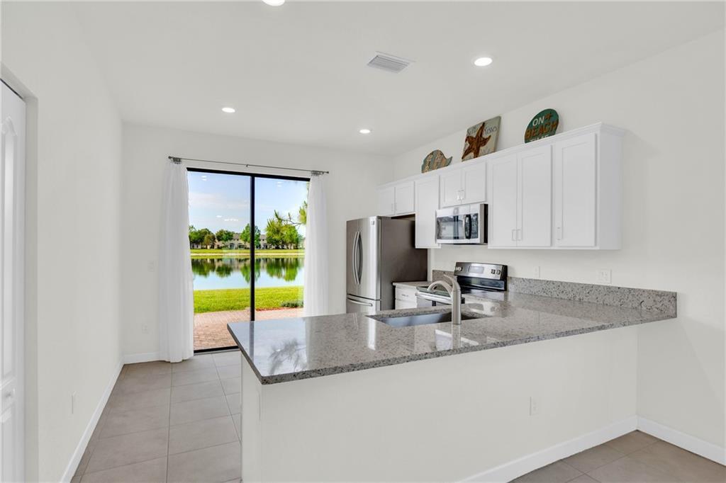 A kitchen with white cabinets, granite countertops, and a sliding glass door overlooking a lake — VERO BEACH, FL