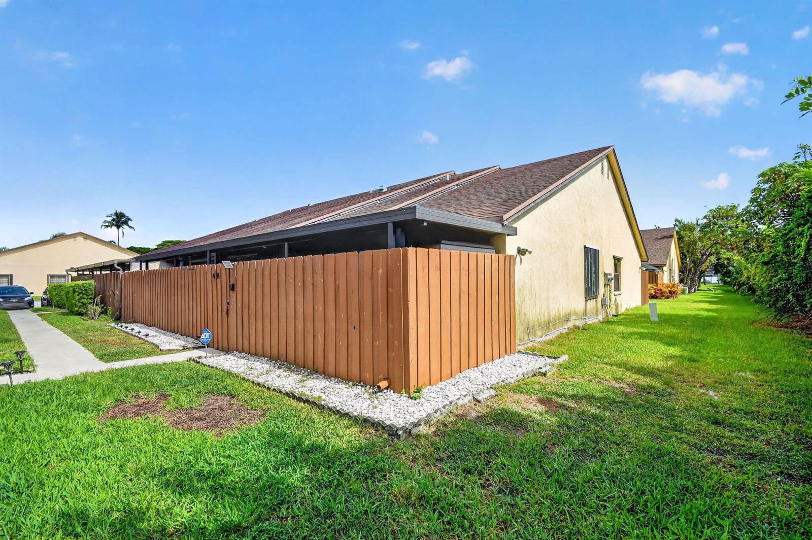 A tan house with a brown wooden privacy fence and a white rock garden border — 414 Springdale Circle, Palm Springs FL 33461, PALM SPRINGS, FL