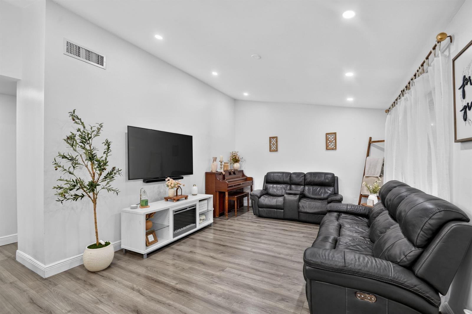 A living room features gray wood-look flooring, white walls, two black leather sofas, and a television — 414 Springdale Circle, Palm Springs FL 33461, PALM SPRINGS, FL