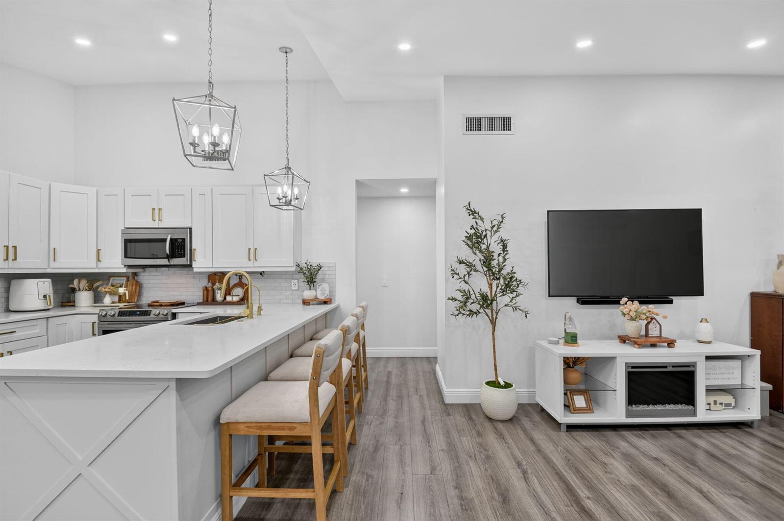 A modern kitchen with white cabinets and a breakfast bar opens into a living area — 414 Springdale Circle, Palm Springs FL 33461, PALM SPRINGS, FL