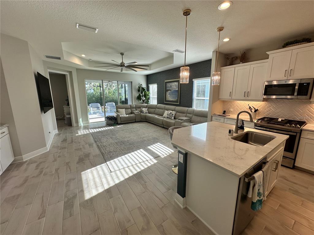 An open-concept kitchen and living area featuring a large island, sectional sofa, and tile flooring — 4727 WILLOW BEND AVENUE, PARRISH, FL