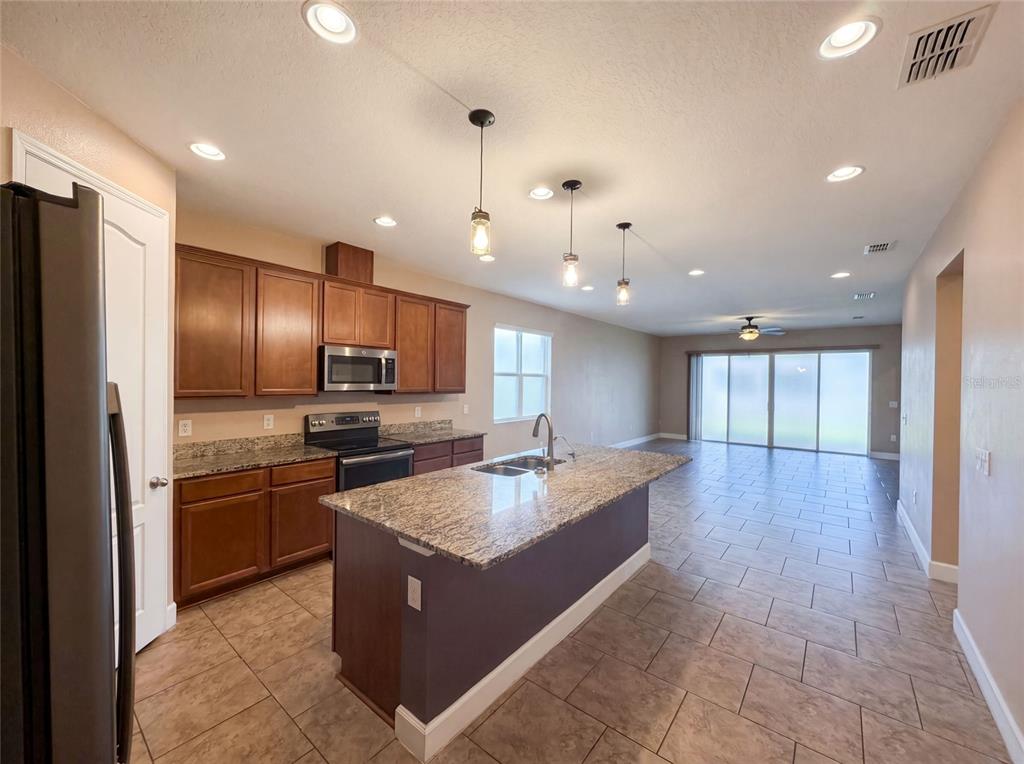 A kitchen with wood cabinets, granite countertops, and an island opens to a tiled living area — 480 BUCHANNAN DRIVE, DAVENPORT, FL