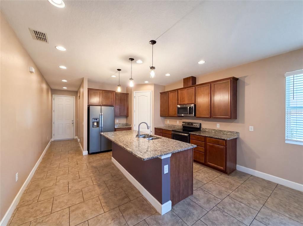 A kitchen features brown cabinets, granite countertops, a central island, and stainless steel appliances — 480 BUCHANNAN DRIVE, DAVENPORT, FL