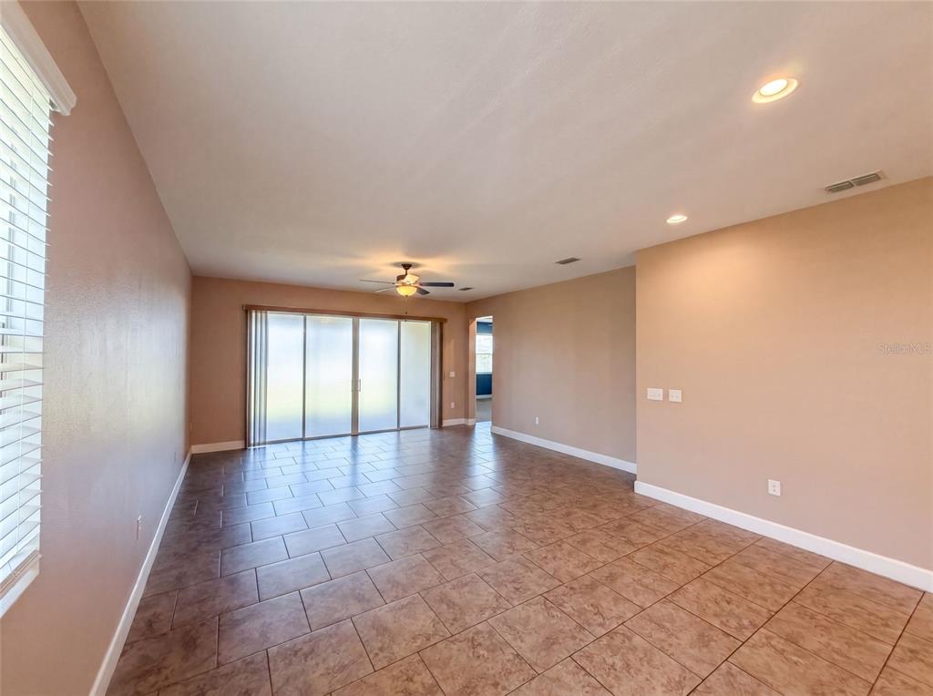 An empty living room features tan walls, tile flooring, a ceiling fan, and sliding glass doors — 480 BUCHANNAN DRIVE, DAVENPORT, FL