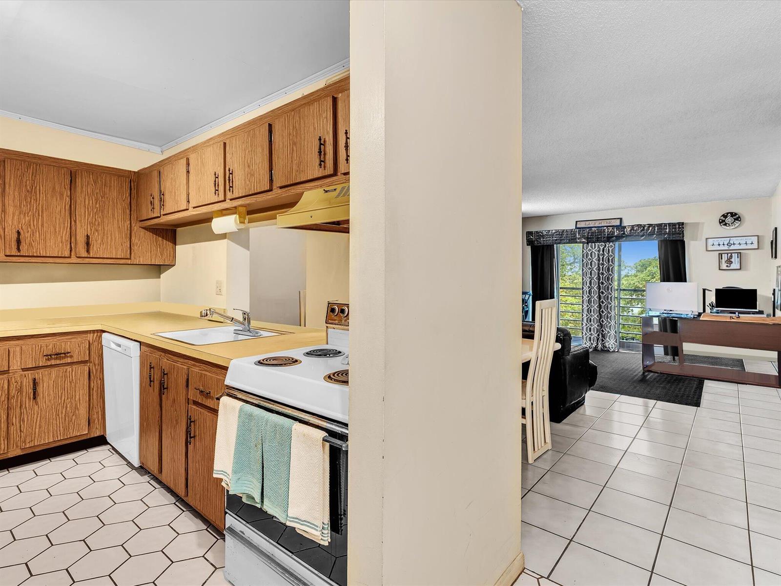 A kitchen with wood cabinets and white appliances opens into a living area with tile floors — 2800 NW 56th # A404, Lauderhill FL 33313, LAUDERHILL, FL