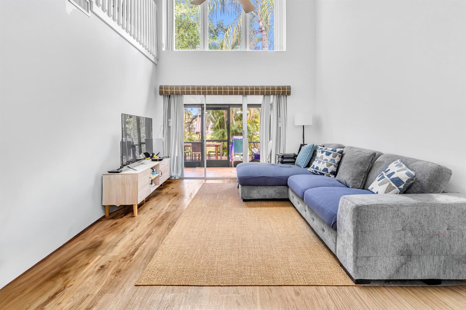 A living room features high ceilings, wood-look flooring, a sectional sofa, and sliding glass doors — 7610 Pinewalk Drive S # 128, Margate FL 33063, MARGATE, FL