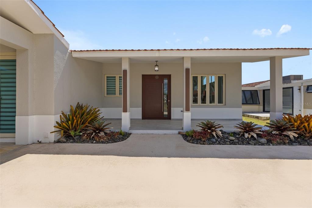The exterior of a modern house features a covered entryway with a dark wood door — 112 CAMINO DE LOS LOTOS, DORADO, PR