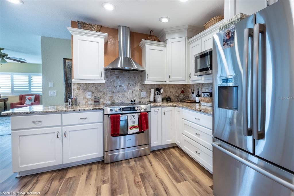 A kitchen features white cabinetry, stainless steel appliances, granite countertops, and wood-look flooring — 1801 JAMAICA WAY UNIT 331, PUNTA GORDA, FL