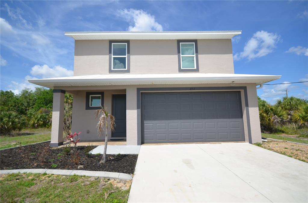 A two-story house with a beige stucco exterior, a gray garage door, and a front porch — 272 PELTON CIRCLE, PORT CHARLOTTE, FL