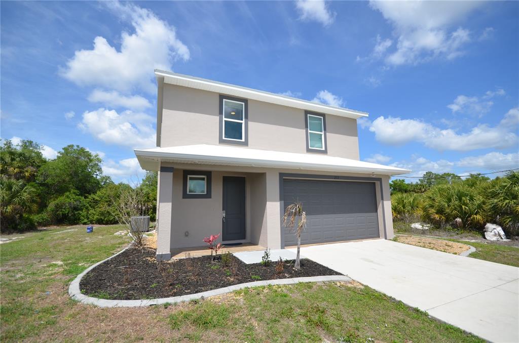 A two-story house with a beige exterior, a gray garage door, and a landscaped front yard — 272 PELTON CIRCLE, PORT CHARLOTTE, FL