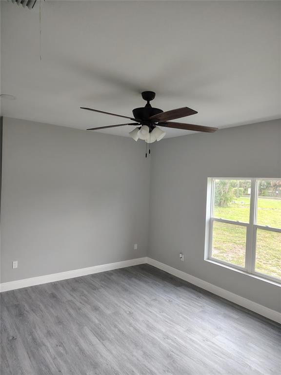 An empty room features gray walls, wood-look flooring, a ceiling fan, and a window — 802 MARVIN C ZANDERS AVENUE, APOPKA, FL