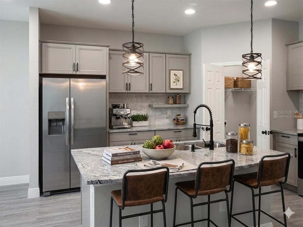 A kitchen features gray cabinets, granite countertops, a central island with bar stools, and stainless appliances — 802 MARVIN C ZANDERS AVENUE, APOPKA, FL