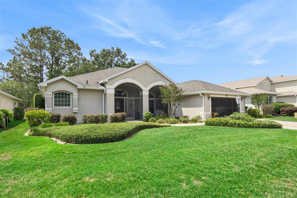 A single-story house with a beige stucco exterior, arched entryway, and a manicured front lawn — 5607 SIR CHURCHILL DRIVE, LEESBURG, FL