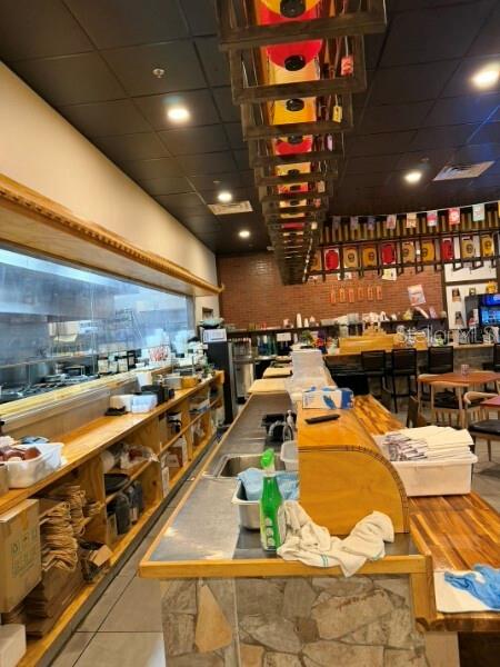 A restaurant interior features a long wooden service counter, open kitchen, and hanging lantern lights — TBA NW 43RD STREET, GAINESVILLE, FL