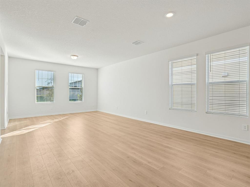 An empty room with light wood-look flooring, white walls, and several windows with blinds — 4688 HOMESTEAD TRAIL, ST CLOUD, FL